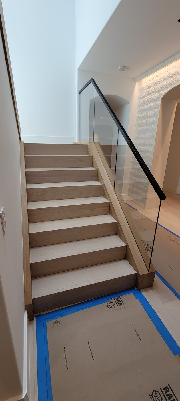 Wood staircase with glass railing beside a stone wall