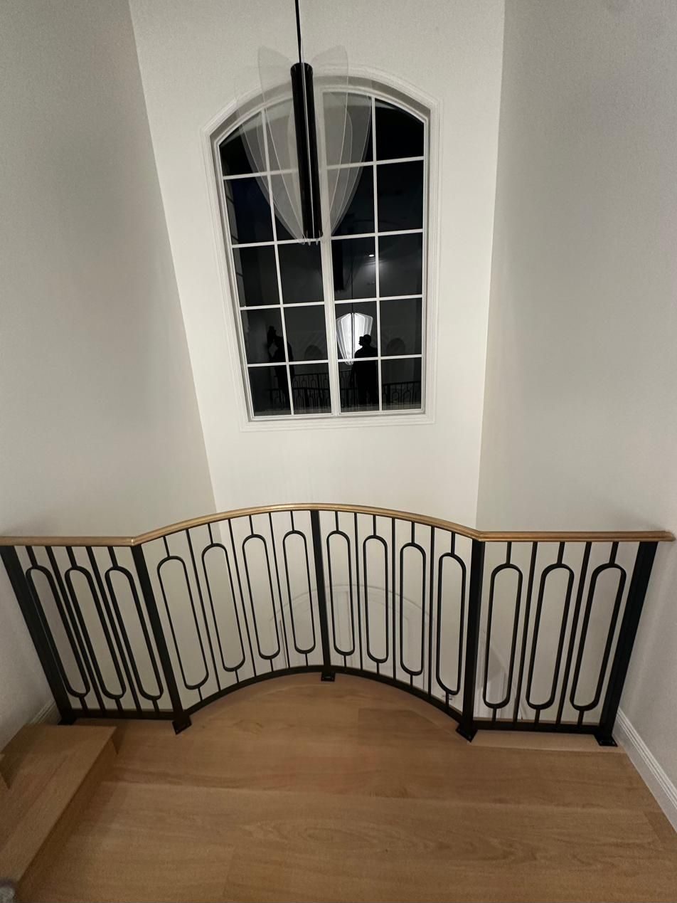 Curved ornamental iron railing with wood cap